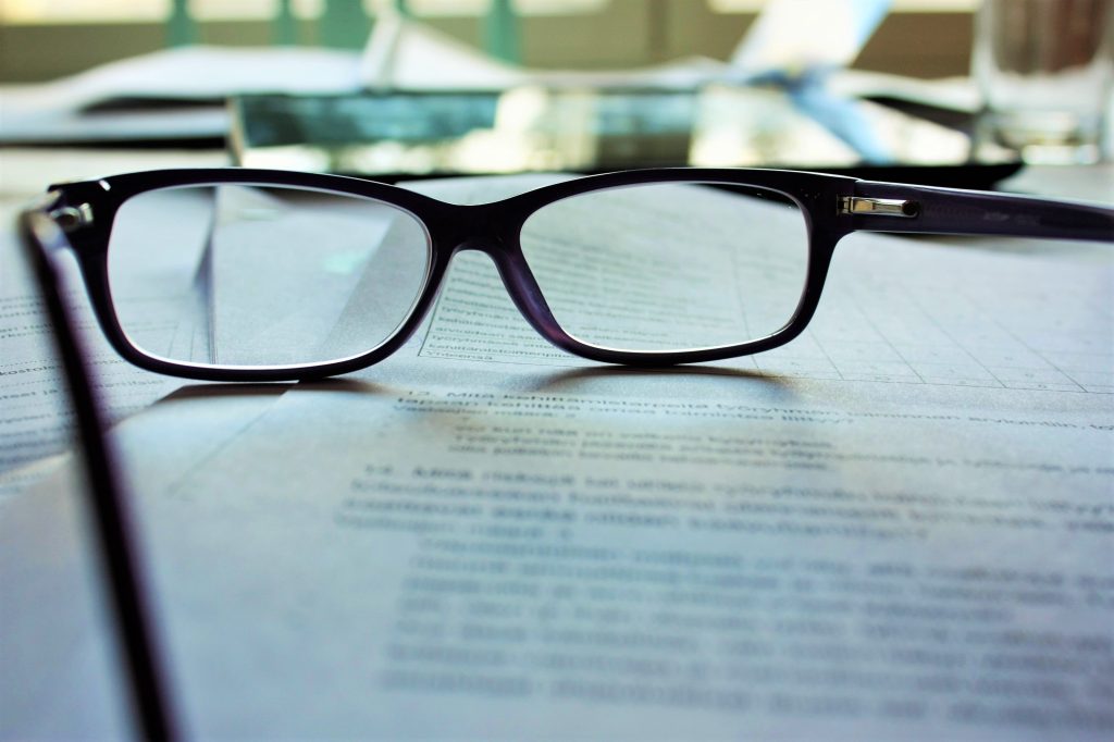 a pair of reading glasses set atop of pile of documents and legal contracts